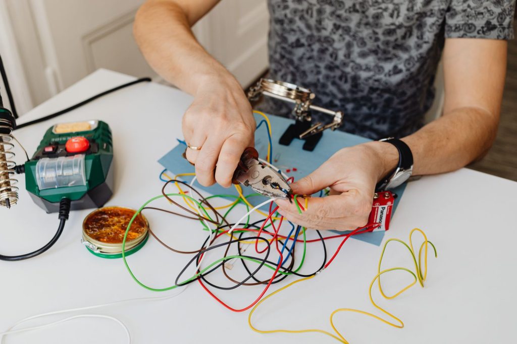 Hands using pliers to strip and repair colored electrical wires