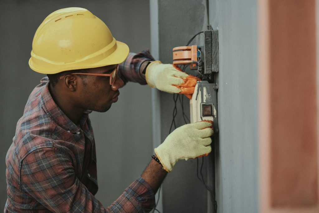 Electrician in a yellow hard hat installing wiring at a wall panel